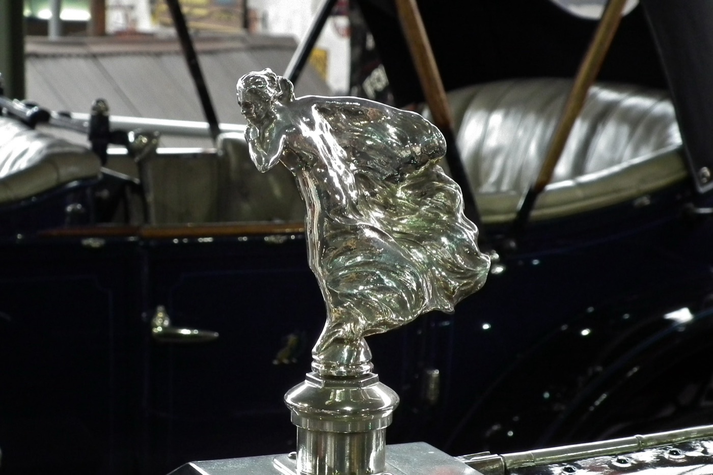 Silver figure of a young woman in windblown robes with a finger raised to her lips, mounted on a radiator cap