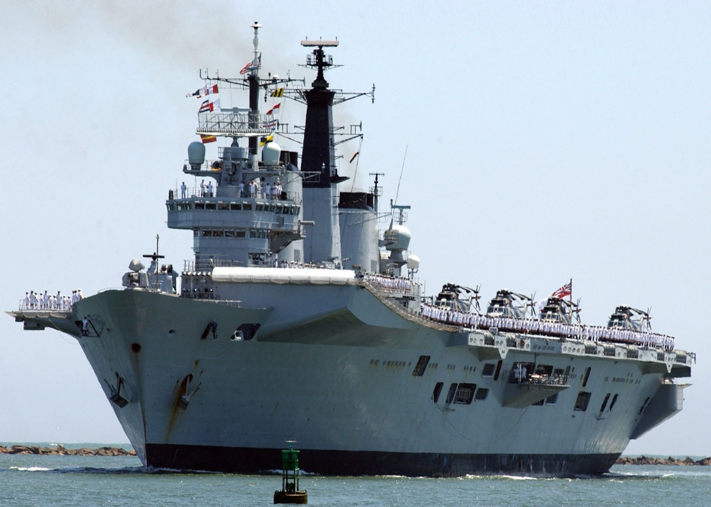 Grey Royal Navy aircraft carrier HMS Invincible at sea, crew lining the flight deck