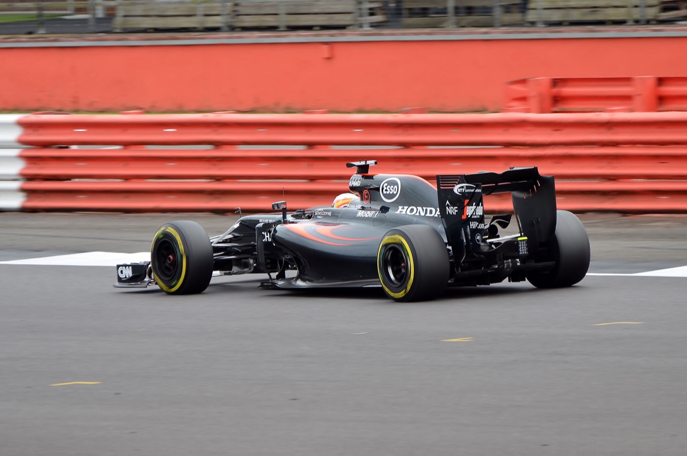 Fernando Alonso in the dark grey McLaren-Honda MP4-31 at Silverstone with red and white barriers behind
