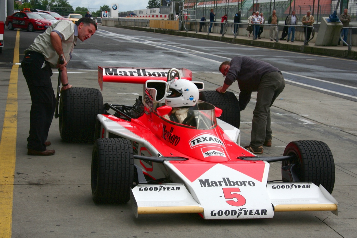 Red and white Marlboro McLaren M23 number 5 once raced by James Hunt, in the Nürburgring pit lane with two men checking its tyres