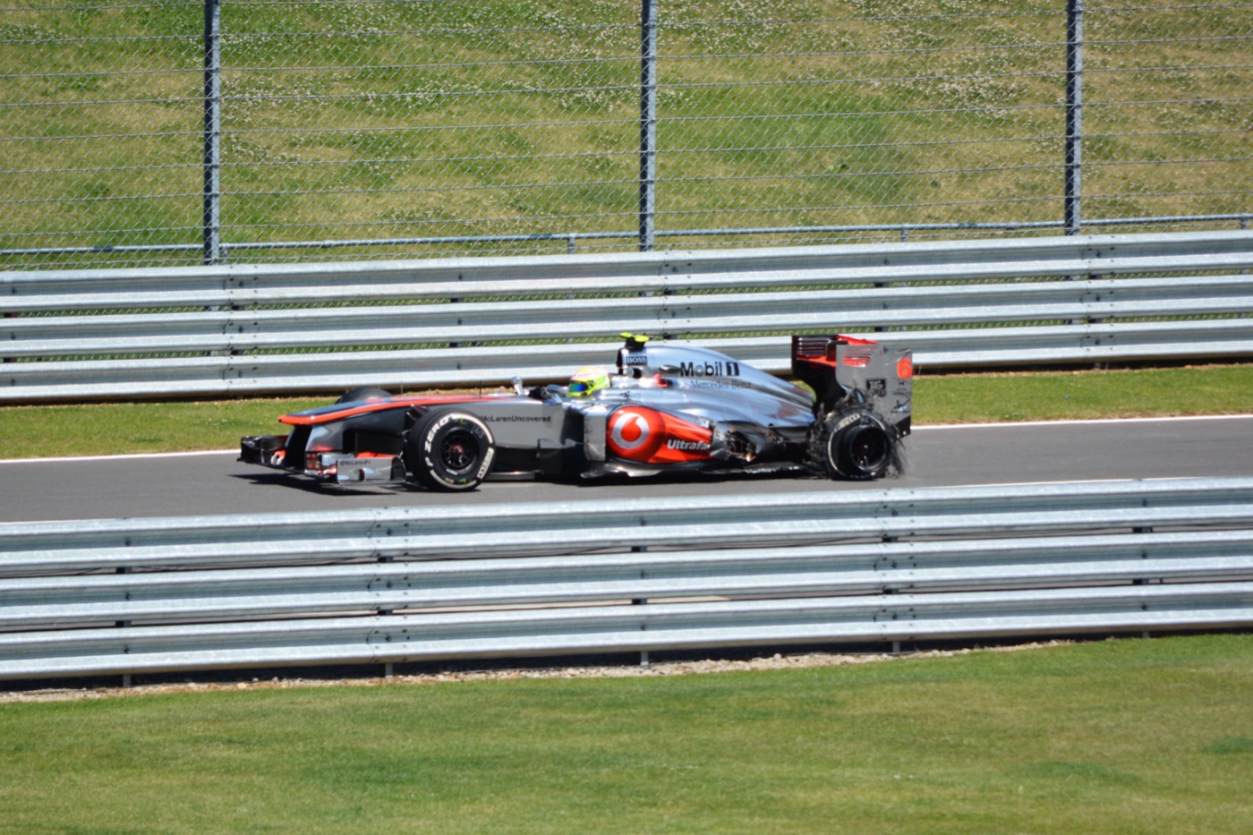Sergio Pérez in the silver McLaren MP4-28 passing a double barrier at Silverstone in sunshine