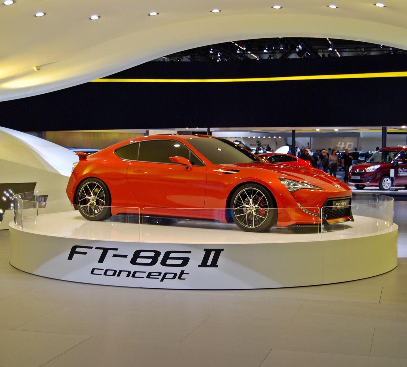 Orange Toyota FT-86 II concept coupe on a round white plinth at a motor show