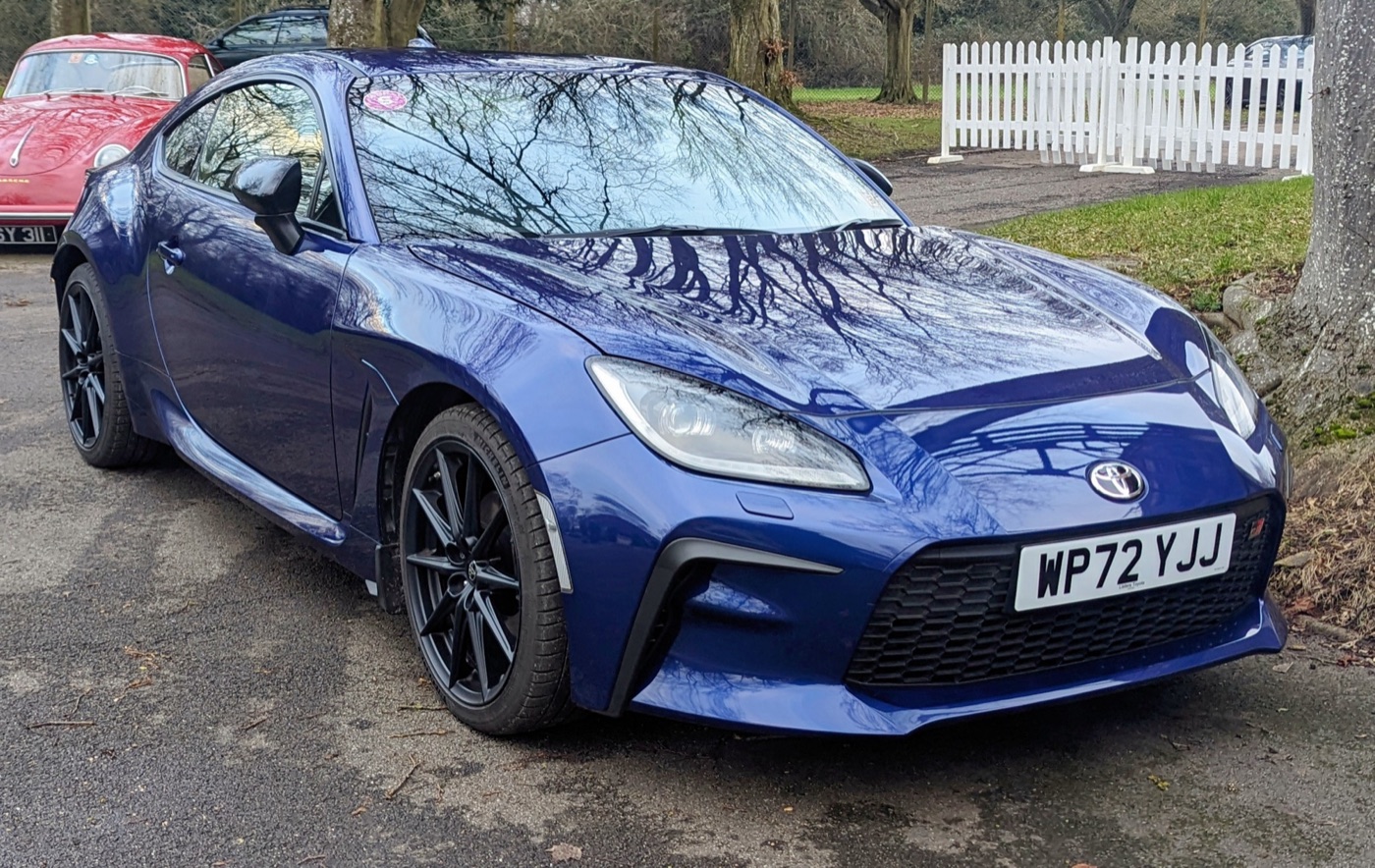 Dark blue Toyota GR86 with black wheels parked by a tree in a car park