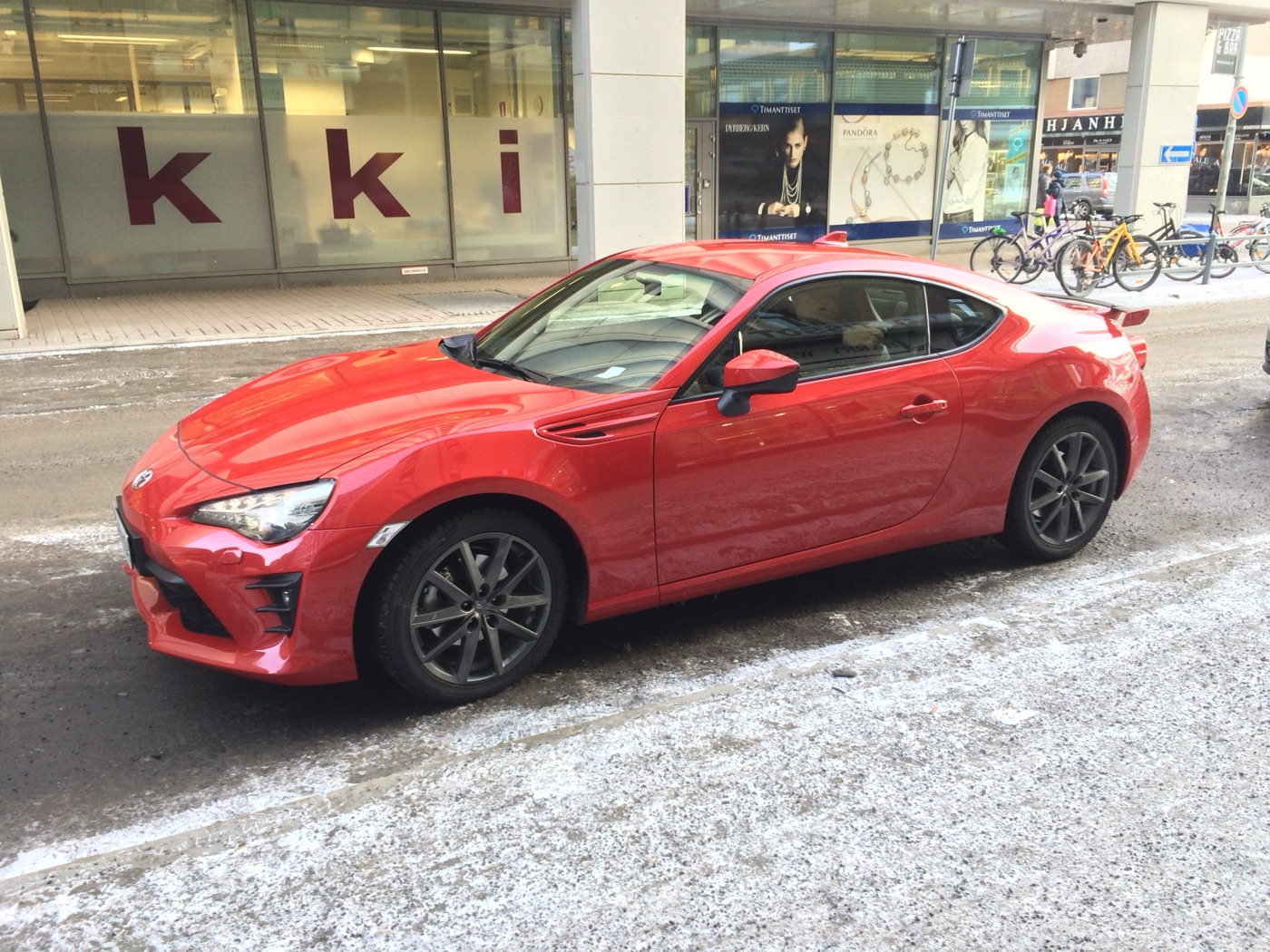 Red facelifted Toyota GT86 with LED headlights and grey ten-spoke wheels parked on a snowy street