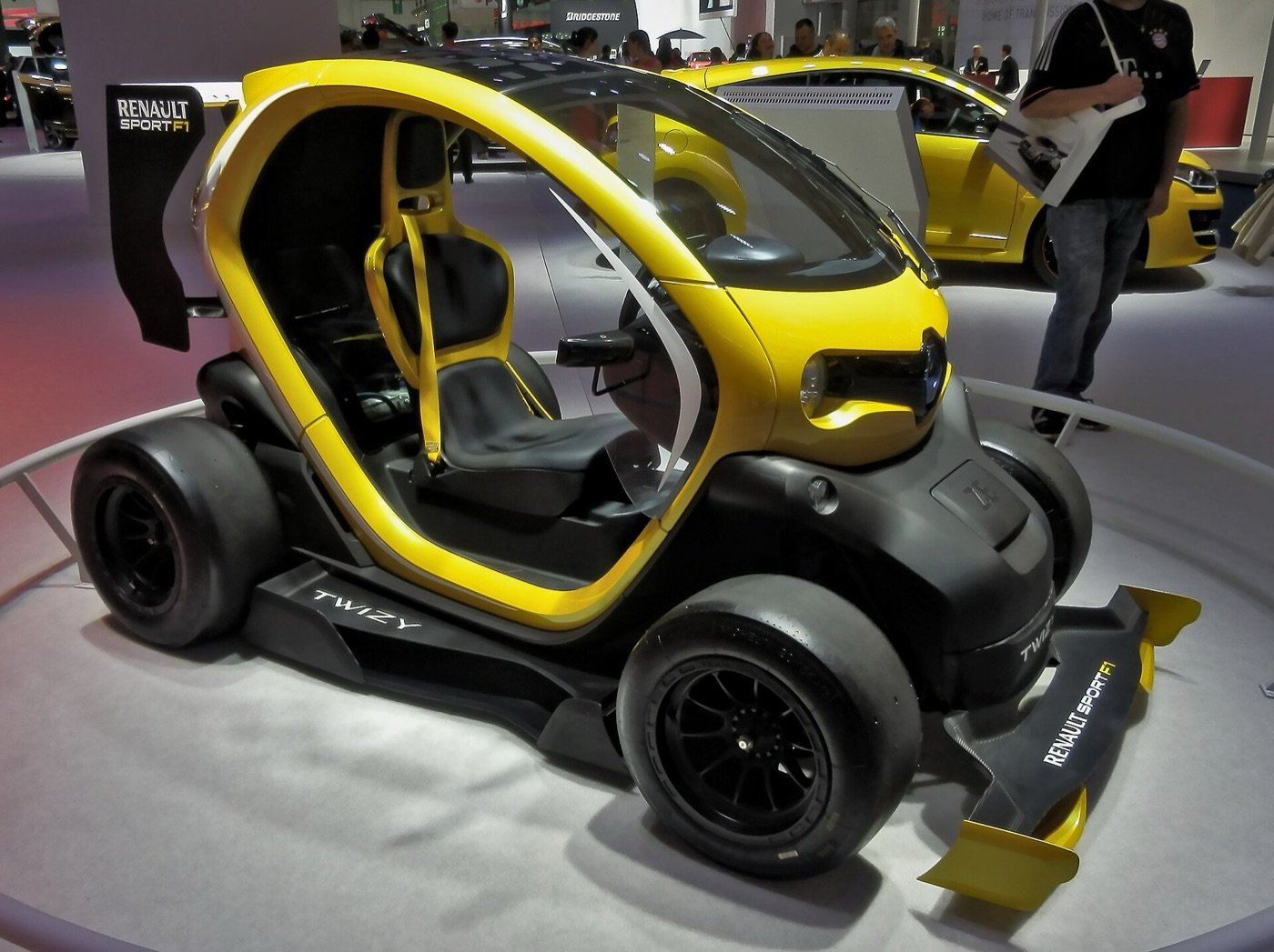 Yellow and black Twizy concept with slick tyres, side pods, a carbon front splitter and a Renault Sport F1 rear wing, on a show stand
