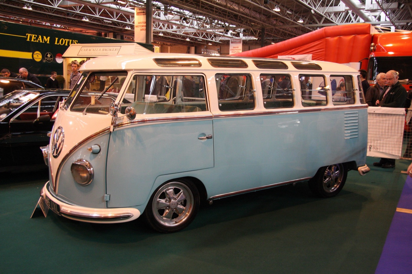 Pale blue and white 1958 Volkswagen T1 Samba with eight roof-edge skylights and curved rear corner windows, at an indoor show