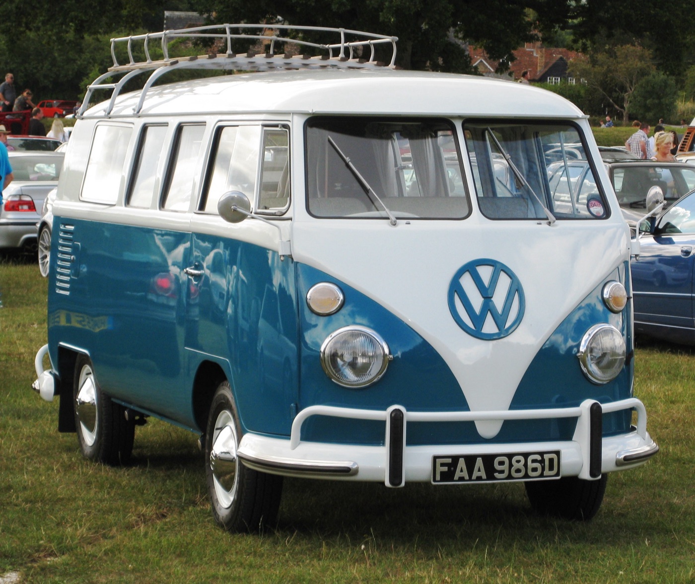 Blue and white 1966 Volkswagen Type 2 T1 split-screen bus with a roof rack and British number plate, seen from the front on grass