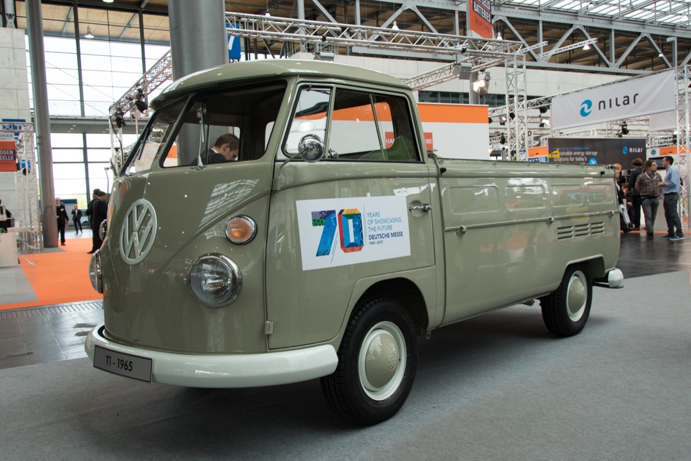 Grey-green 1965 Volkswagen T1 single-cab pickup on display in an exhibition hall