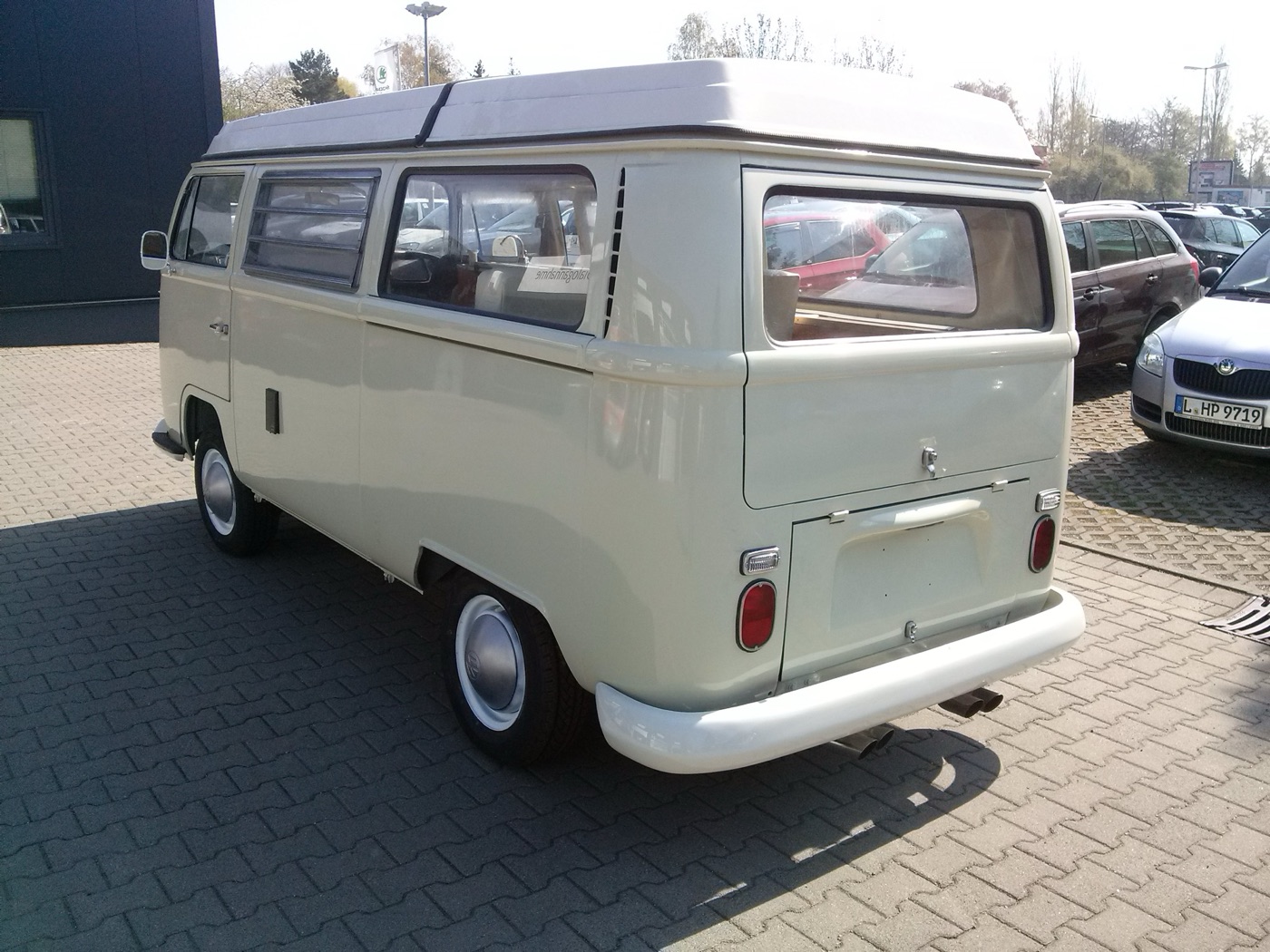 Cream early bay-window Volkswagen T2 Westfalia camper with an elevating roof, seen from the rear left with small round tail lights