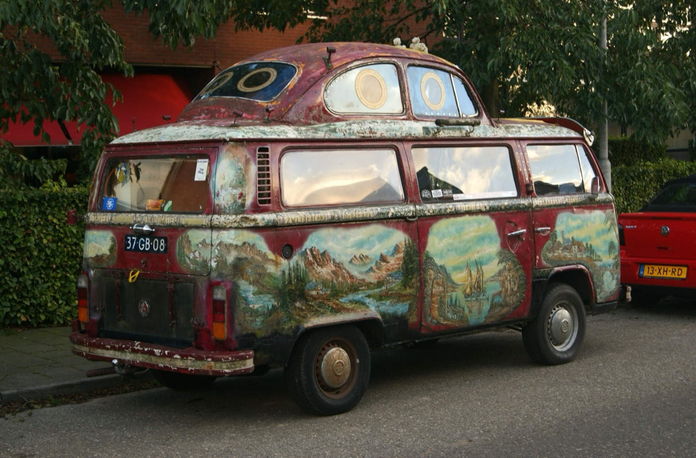 Weathered 1978 Volkswagen T2 bay-window bus hand-painted with mountain and lake scenes, with the body of a Beetle welded onto its roof