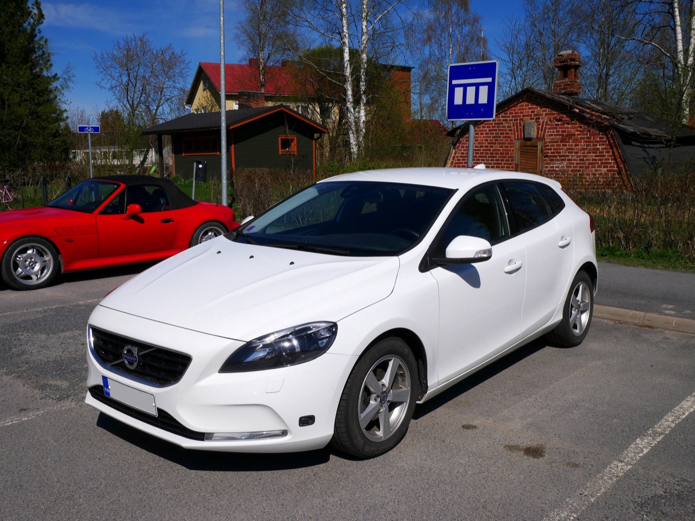 White pre-facelift Volvo V40 D2 hatchback with five-spoke alloy wheels in a car park, a red convertible behind