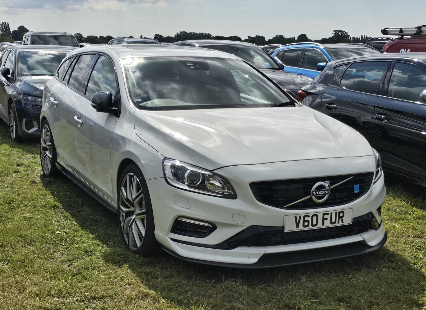 White 2018 Volvo V60 Polestar estate with dark front splitter and 20-inch wheels, parked on grass