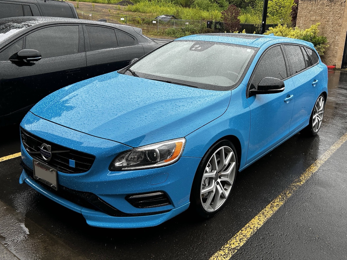 Rebel Blue Volvo V60 Polestar estate from the front three-quarter on a wet car park, with 20-inch Polestar wheels and splitter