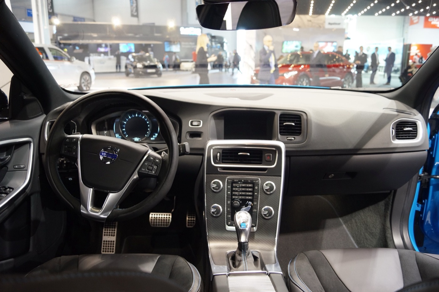 Dashboard and front seats of a Volvo S60 Polestar with blue-stitched charcoal seats, sports pedals and a lit gear lever