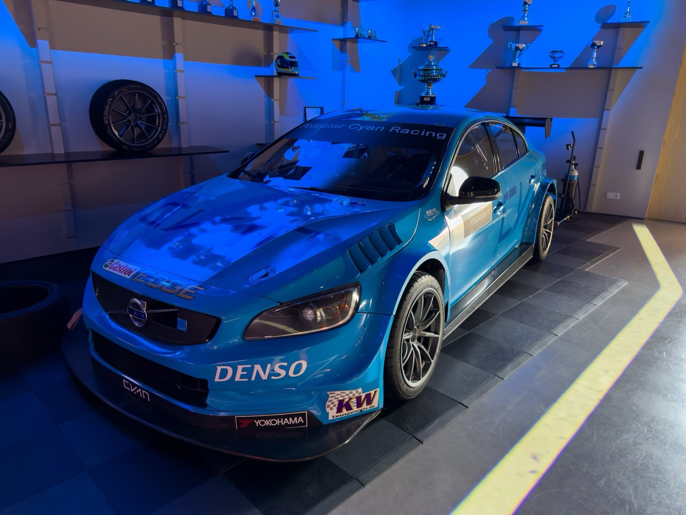 Blue Volvo S60 Polestar TC1 touring car in Cyan Racing livery with Denso and Yokohama decals, displayed indoors