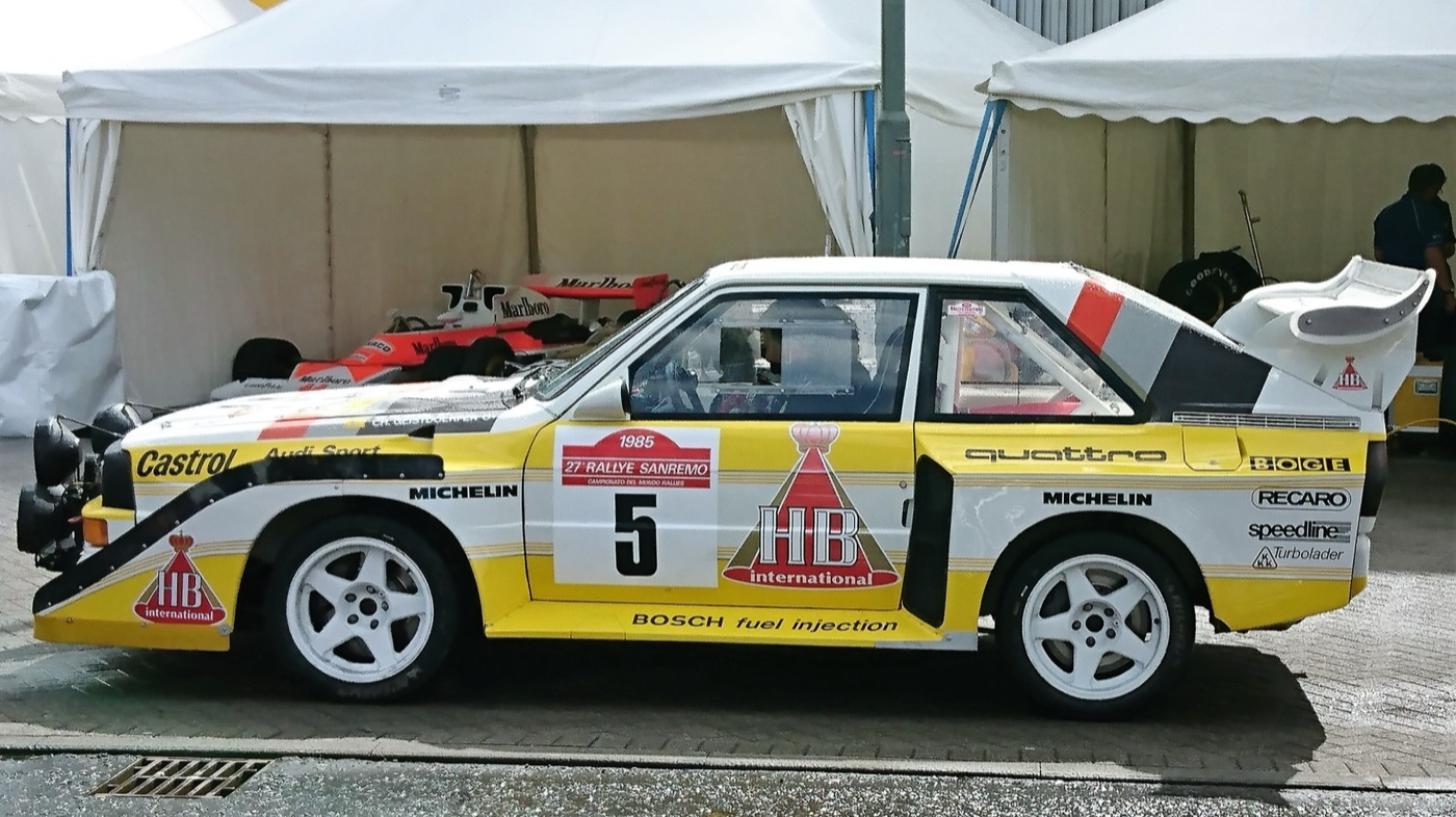 Yellow and white Audi Sport Quattro S1 E2, number 5, with a large rear wing, parked under a white tent