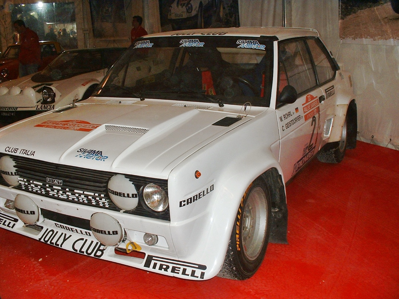 White Fiat 131 Abarth rally car in Jolly Club colours with Pirelli and Cibié lamps, Röhrl and Geistdörfer named on the side