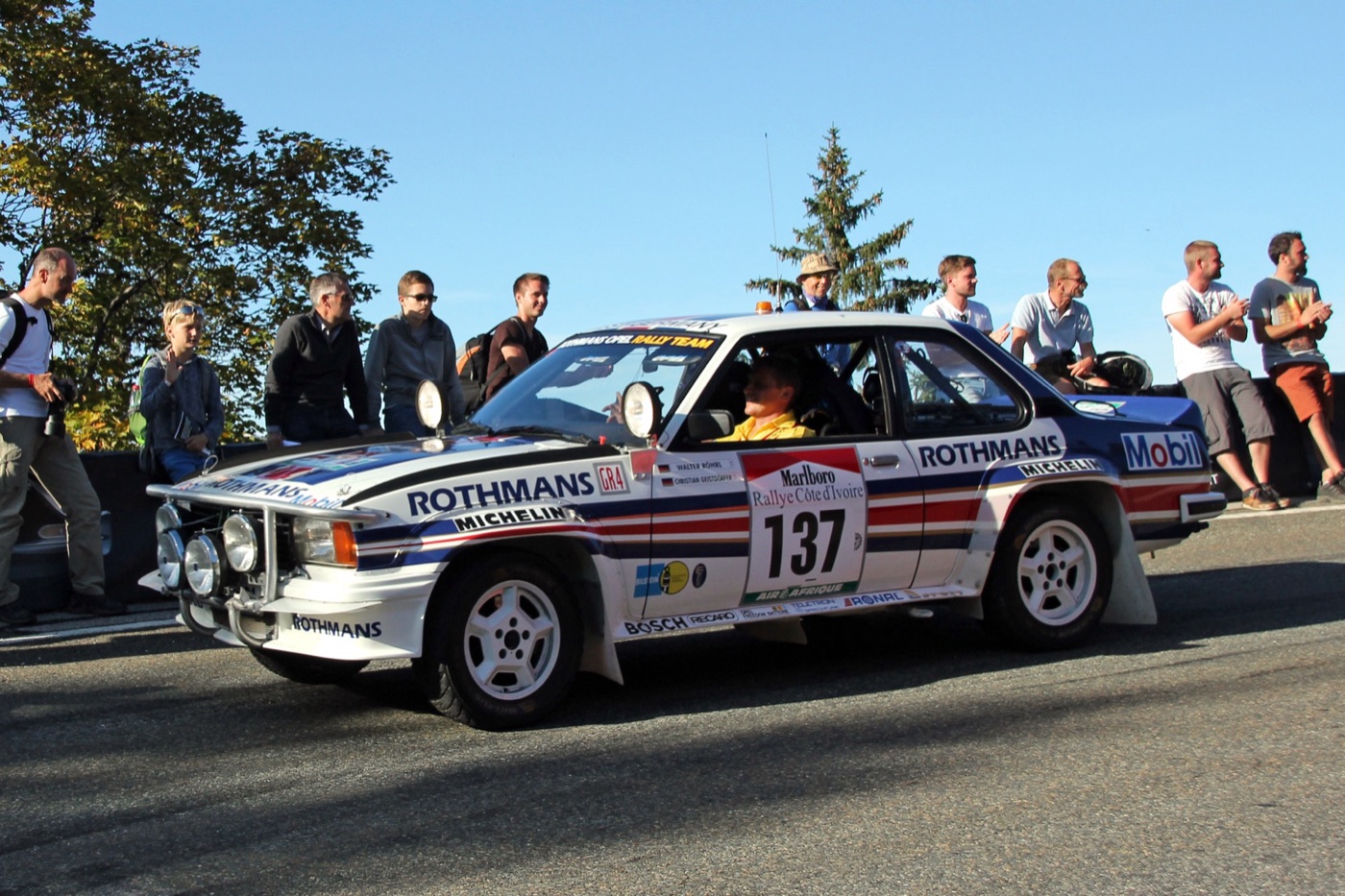 White Opel Ascona 400 in Rothmans colours, number 137, with spotlights, driving past spectators