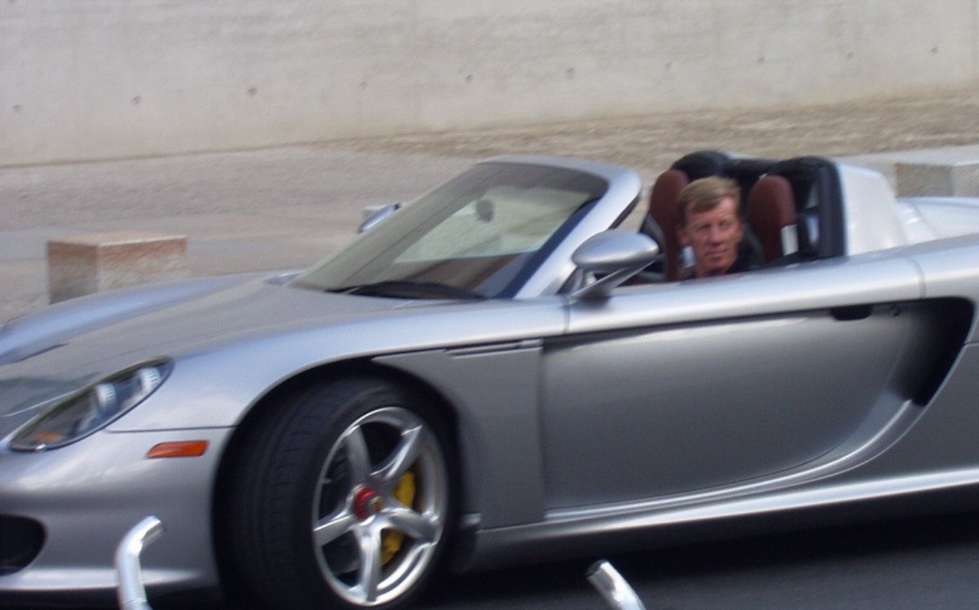 Walter Röhrl at the wheel of a silver Porsche Carrera GT roadster with its roof off