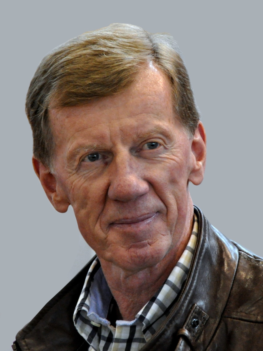 Walter Röhrl, grey-haired and smiling, in a brown leather jacket and checked shirt