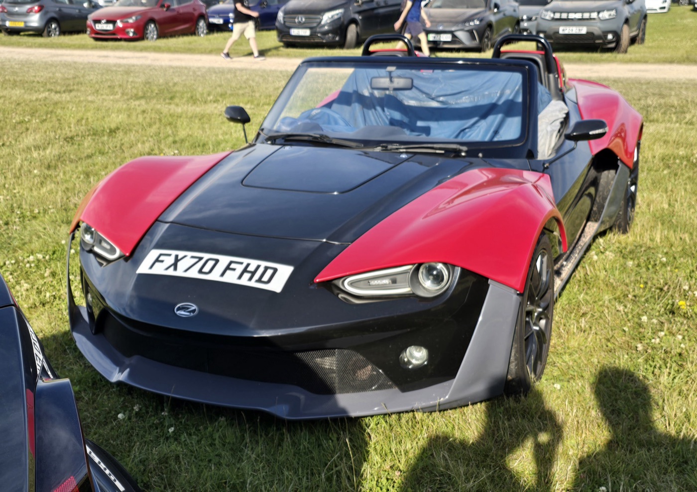 Red and black Zenos E10 with a 2020 registration plate parked on grass at a show